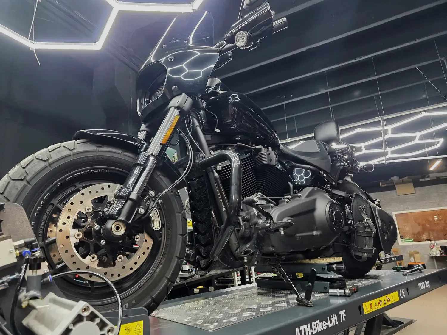 Motocykle Harley-Davidson na podnośnikach pod sześciokątnym oświetleniem w warsztacie Heavyweight Garage w Gdyni